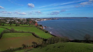 Holcombe, Güney Devon, İngiltere: DRONE VİEWS: İHA bir tepenin üzerinden kıyı şeridine doğru uçuyor ve orta alandaki Dawlish kasabasını gösteriyor. Dawlish, siyah kuğu nüfusuyla ünlü popüler bir İngiliz turizm şehridir (2. klip 2).).