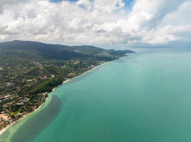 Turkuaz sularla geniş kıyı manzarası, yemyeşil yemyeşil ve güneşli bir gökyüzünün altında uzak ufuklar. Koh Samui, Tayland.
