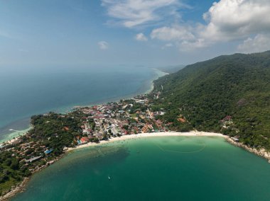 Bereketli yeşil tepeler, açık mavi gökyüzünün altında tropikal bir sahil şeridi boyunca turkuaz denizle buluşuyor. Ko Pha Ngan, Tayland.