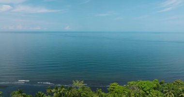Sahilde güzel okyanus dalgaları olan tropik bir ada. Mavi deniz ve bulutlu açık gökyüzü. Mindanao, Filipinler.