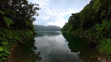 Yağmur ormanı yamaçlarının arasında berrak su ve bulutlu gökyüzü yansıması olan sessiz bir göl. Siargao, Filipinler.