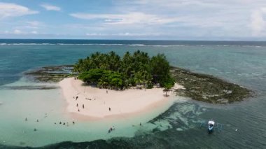 Turistler palmiye ağaçları olan küçük kumlu bir adanın yakınında yüzüyor ve dinleniyorlar. Guyam Adası. Siargao, Filipinler.