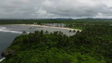 Gökyüzü bulutlu palmiye ağaçları ile çevrili kumlu sahil boyunca bir köy. Siargao, Filipinler.