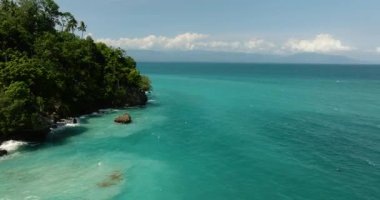 Kıyı sahili, kayalar ve okyanus dalgaları. Mavi gökyüzü ve bulutların altında turkuaz su. Samal Adası. Davao, Filipinler.