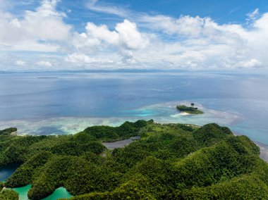 Verdant kıyı tepeleri, açık turkuaz su ve mercan oluşumlarıyla çevrili küçük bir tropikal adanın bulunduğu denize doğru uzanır. Siargao, Filipinler. Sugba Mavi Göl.