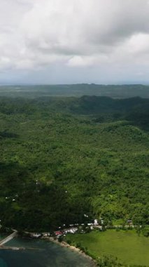 Sahil şeridinde yeşil tepeler ve kıyıya yakın bulutlu bir atmosfer olan bir kasaba. Siargao, Filipinler.