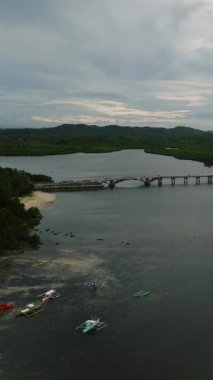 Sahil şeridi yakınlarında yeşil bitki örtüsüyle çevrili sakin bir nehir boyunca uzanan beton bir köprü. Siargao, Filipinler.