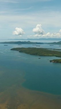 Tropik ada ve kargo gemisi mavi gökyüzü ve bulutların altında. Mindanao, Filipinler. Dikey görünüm.