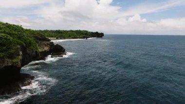 Okyanus dalgaları yoğun tropikal ormanlarla çevrili kayalık kayalıklara çarpıyor. Siargao, Filipinler.