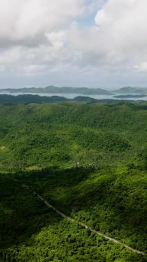 Yoğun ormanlarla kaplı tropikal dağ sırtları dramatik bulut gölgelerinin altında ve uzaktan görülebilen deniz. Siargao, Filipinler.