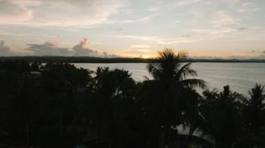 Akşam gökyüzü, kıyı şeridinin üzerinde günbatımı renkleriyle ve ufukta palmiye ağaçlarının siluetleri. Siargao, Filipinler.