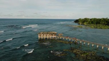İskeledeki ahşap kulübe. Etrafı dalgalarla çevrili. Kayalıklarda ve okyanustaki sörfçülerle. Siargao, Filipinler. Bulut 9 Sörf Alanı.