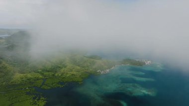 Yeşil tepeleri kıyı suyuyla kaplayan alçak sürüklenen bulutlar kıyı boyunca uzanan küçük köyler. Siargao, Filipinler.