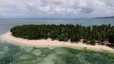 Palmiye ağaçlarıyla kaplı kıvrımlı kumlu sahil parlak gökyüzünün altında turkuaz sığ sularla buluşuyor. Siargao, Filipinler. Casa Desideria.