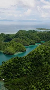 Orman adaları ve tepeler görülebilir tekne ve kıyı şeritleriyle çevrili sakin mavi bir göl. Sugba Mavi Göl, Siargao, Filipinler.