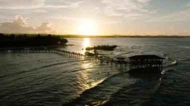 Ahşap iskele ve kulübe, suya yansıyan günbatımı ışığıyla birlikte denize doğru uzanıyor. Siargao, Filipinler. Bulut 9 Sörf Alanı.