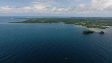 Mavi açık deniz, küçük yeşil adaları olan bir kıyı şeridiyle birleşir ve uzaktaki ormanlık alanla birleşir. Siargao, Filipinler.