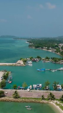 Açık bir gökyüzünün altında tekneler, yeşil tepeler ve tropikal bitkilerle çevrili pitoresk bir liman. Ko Pha Ngan, Tayland.