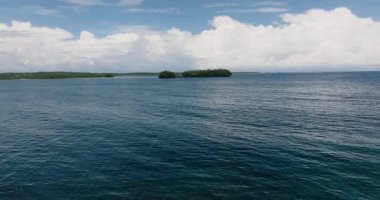 Bulutlu gökyüzünün altında mavi okyanus suyuyla çevrili küçük yeşil bir ada. Siargao, Filipinler.