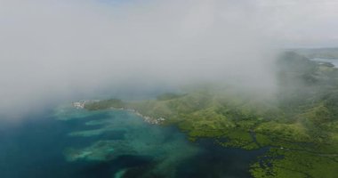 Yeşil kıyı şeridi boyunca mercan kayalıkları ve deniz kıyısında alçak bulutlar olan bir köy. Siargao, Filipinler.