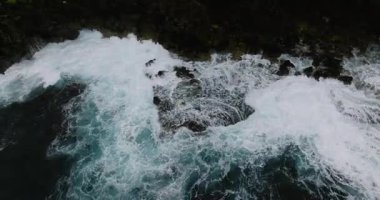 Köpüklü dalgalar engebeli sahil boyunca kayaların üzerine turkuaz suyla çarpıyor. Siargao, Filipinler.