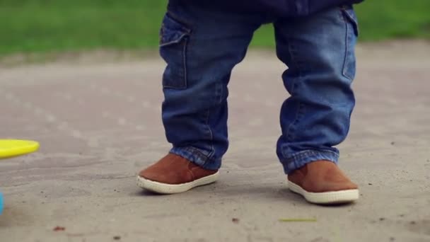 Lindo niño pequeño en pantalones vaqueros azules caminando cerca de monopatín. Patas de bebé — Vídeos de Stock