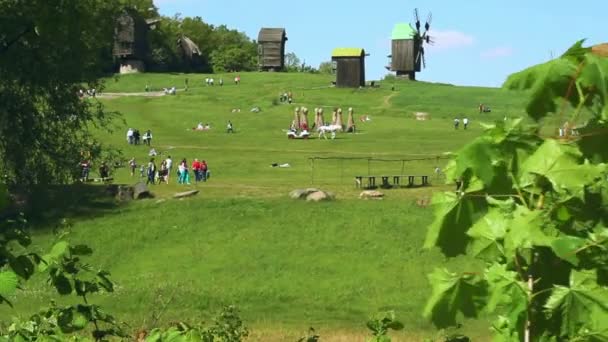 Люди отдыхают на зеленом лугу в весеннем парке. Зеленые деревья и старая мельница — стоковое видео