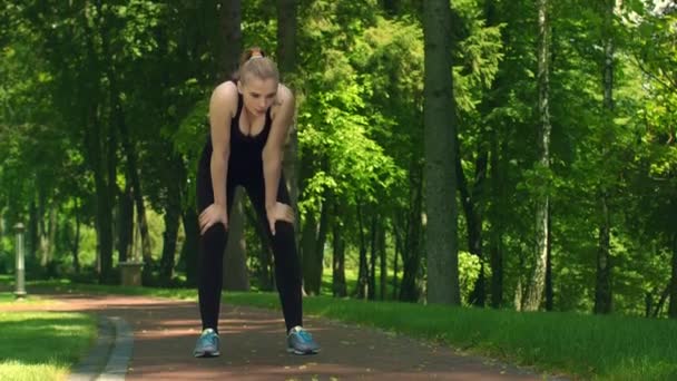Κουρασμένος γυναίκα ανάπαυση μετά το τρέξιμο σκληρά στο πάρκο. Κορίτσι Fit χαλαρώστε μετά από τρέξιμο — Αρχείο Βίντεο