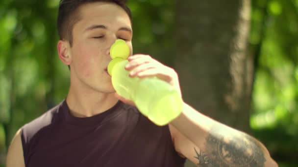 Moe sport man drinkt water uit plastic fles na marathon in park — Stockvideo