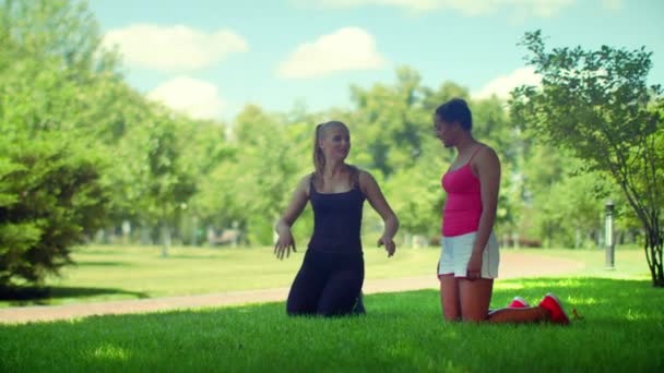 Fit girls talking kneeling on green grass in park — Stock Video