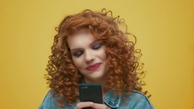 Akıllı telefondan mesaj atan bir kadın. Sarı arkaplanda cep telefonu kullanan kız