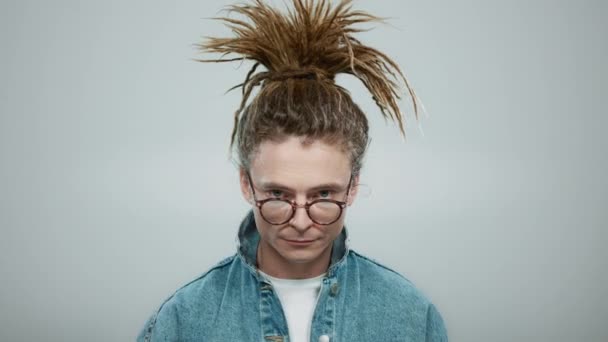 Elegante hipster em pé sobre fundo cinza. Focado cara colocando em óculos — Vídeo de Stock