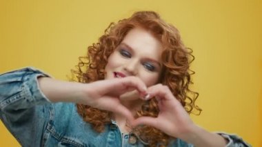 Kalp belirtisi gösteren bir kadın. Sarı arka planda aşk sembolü gösteren kız