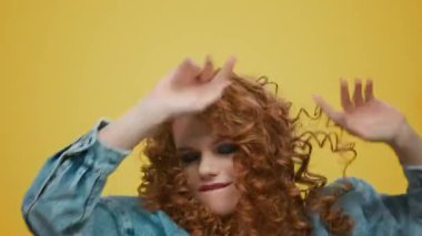 Stüdyoda dans eden gülümseyen kadın. Sarı arka planda zıplayan oyuncu kız