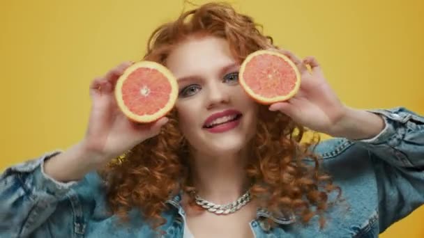 Een vrouw met stukjes grapefruit. Meisje bedekt gezicht met grapefruit helften — Stockvideo