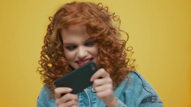Sarı arka planda akıllı telefondan oyun oynayan bir kadın. Telefonu kullanan şık bir kız.