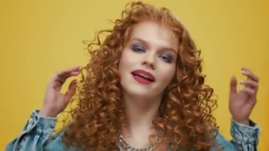 Sarı arka planda kamerayla flört eden bir kadın. Saça dokunan pozitif kız