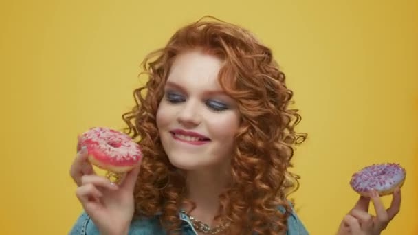 Позитивная девушка держит пончики на желтом фоне. Счастливая дама пробует пончик — стоковое видео
