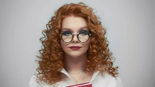 Woman in glasses standing in studio. Portrait of female student holding book