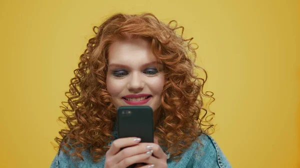 Menina chocada lendo más notícias no celular no fundo amarelo — Fotografia de Stock