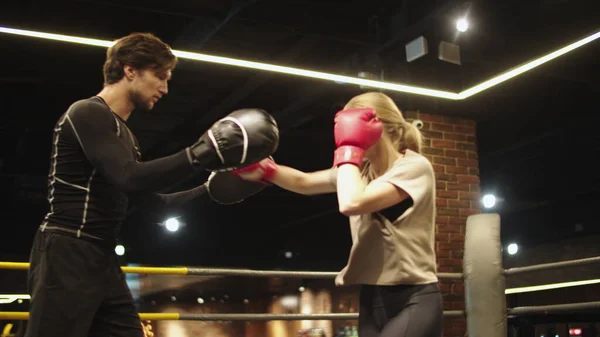 Mujer deportiva enojada entrenando con entrenador en el gimnasio. Chica en forma luchando en el ring de boxeo — Foto de Stock