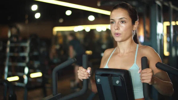 Sporty girl doing arm exercises at gym. Woman using simulator in sport club