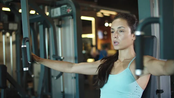 Chica bastante en forma usando simulador en el club deportivo. Mujer haciendo rizos bíceps en el gimnasio — Foto de Stock