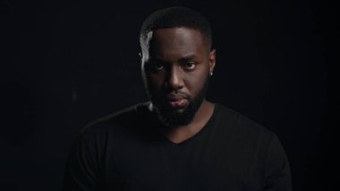 Kapalı alanda kameraya bakan sıkı bir afro adam. Ciddi bir Afrikalı el ele tutuşuyor.