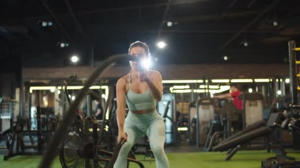 Menina desportiva usando cordas de batalha no clube desportivo. Fit menina fazendo crossfit no ginásio — Vídeo de Stock