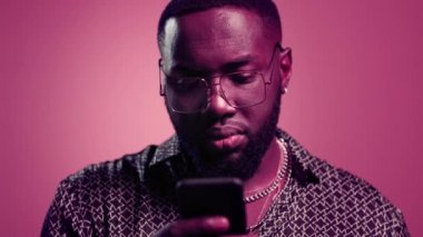 Stüdyoda afro adam mesaj okuyor. Pembe arka planda akıllı telefon kullanan adam