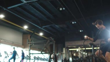 Formda bir adam kulüpte kardiyo yapıyor. Spor adamı spor salonunda velosimulatör kullanıyor.