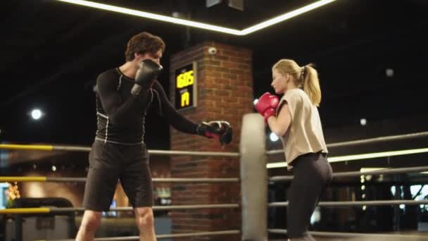 Amistoso entrenador enseñando chica en forma en el ring de boxeo. Los oponentes boxeo en el gimnasio — Vídeos de Stock
