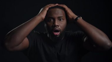 Siyah arka planda poz veren stresli afro adam. Kapalı alanda el ele tutuşan adam.
