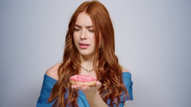 Mujer dudosa sosteniendo donuts en el interior. Chica tratando de no comer en el estudio — Vídeo de stock